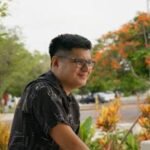 Portrait of a man with glasses smiling in a vibrant park setting in Merida, Yucatan, Mexico.